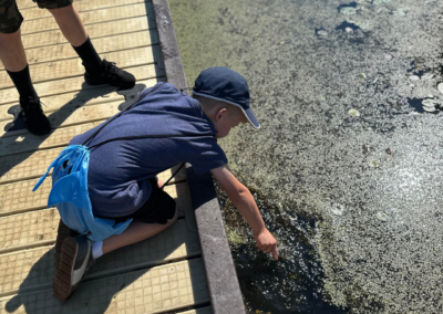 A child crouching on a dock at outdoor therapy camp to play in the water. Arlington Heights, Rolling Meadows, Palatine, and surrounding areas.