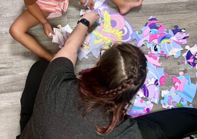 A photo of one of our speech therapists working with a child on a puzzle. the photo is taken from above so it is an ariel view of the therapist, the child, and a my little pony puezzle.