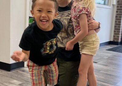 One of our occupational therapists, Sam, is hugged by two children during an occupational therapy session. Everyone is smiling big in the photo.