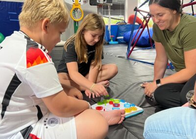 One of our occupational therapists, Michaela, plays a game with two kids during an occupational therapy session. The two children are moving game pieces on the board as Michaela smiles.